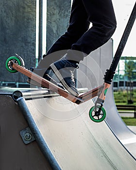 Teenager boy rides on kick scooter in outdoor skatepark. Summer extreme sports competition outside. Feet of male teen riding on