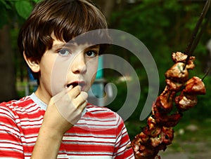 Teenager boy with roasted beef meat shashlik on braiser iron skewer