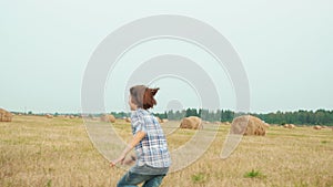 Teenager boy running on farming field on haystack background. Girl teenagers sitting on haystack on harvesting field in