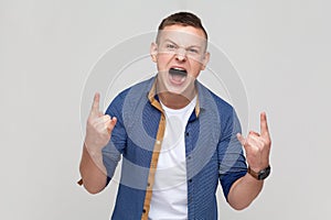 Teenager boy showing rock and roll hand gesture, crazy devil horns with fingers and yelling.