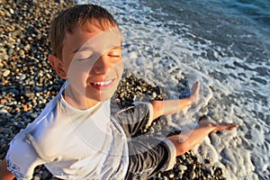 Teenager boy sit on stone seacoast, closed eyes