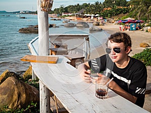 Teenager boy is sitting at a beach bar and is playing on mobile device