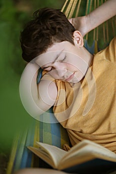 Teenager boy sleeping while reading in hammock