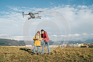 Teenager boy son dressed yellow jacket and Father piloting a modern digital drone using remote controller. Modern technology