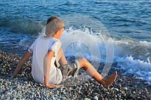 Teenager boy on stone seacoast, wets feet in water photo