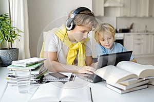 Teenager boy study at home. His younger brother is playing near. Homeschooling. Online education and distance learning for