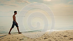 Teenager boy walking along the beach at sunset.