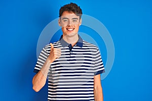 Teenager boy wearing casual t-shirt standing over blue  background doing happy thumbs up gesture with hand