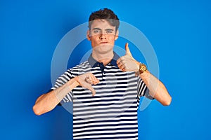 Teenager boy wearing casual t-shirt standing over blue  background Doing thumbs up and down, disagreement and agreement