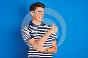 Teenager boy wearing casual t-shirt standing over blue  background Looking proud, smiling doing thumbs up gesture to the