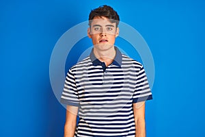 Teenager boy wearing casual t-shirt standing over blue  background looking sleepy and tired, exhausted for fatigue and