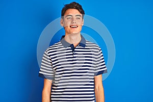 Teenager boy wearing casual t-shirt standing over blue  background smiling looking to the side and staring away thinking