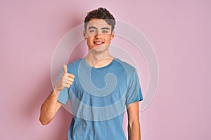 Teenager boy wearing casual t-shirt standing over blue isolated background doing happy thumbs up gesture with hand