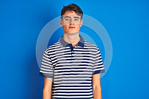 Teenager boy wearing casual t-shirt standing over blue isolated background Relaxed with serious expression on face