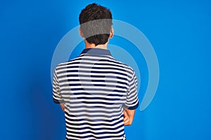 Teenager boy wearing casual t-shirt standing over blue isolated background standing backwards looking away with crossed arms