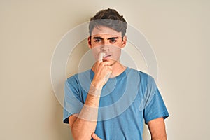 Teenager boy wearing casual t-shirt standing over isolated background looking stressed and nervous with hands on mouth biting