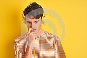 Teenager boy wearing headphones over  yellow background looking stressed and nervous with hands on mouth biting nails