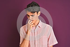 Teenager boy wearing pink shirt standing over purple isolated background looking stressed and nervous with hands on mouth biting