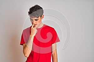 Teenager boy wearing red t-shirt over white isolated background looking stressed and nervous with hands on mouth biting nails