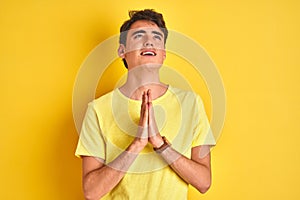 Teenager boy wearing yellow t-shirt over  background begging and praying with hands together with hope expression on face