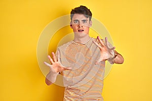 Teenager boy wearing yellow t-shirt over isolated background afraid and terrified with fear expression stop gesture with hands,
