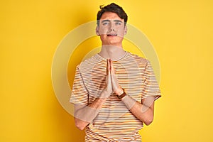 Teenager boy wearing yellow t-shirt over isolated background begging and praying with hands together with hope expression on face