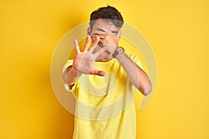 Teenager boy wearing yellow t-shirt over isolated background covering eyes with hands and doing stop gesture with sad and fear