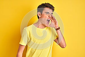 Teenager boy wearing yellow t-shirt over isolated background shouting and screaming loud to side with hand on mouth