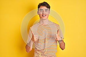 Teenager boy wearing yellow t-shirt over isolated background success sign doing positive gesture with hand, thumbs up smiling and