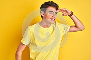 Teenager boy wearing yellow t-shirt over isolated background very happy and smiling looking far away with hand over head