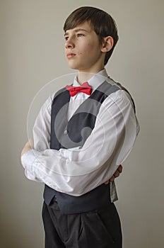 Teenager boy in a white shirt and a waistcoat with the red bow tie