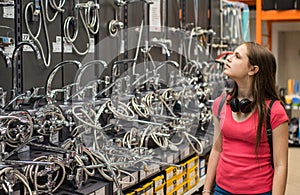 Teenager brunette girl in coral t-shirt with long hair choosing a bathroom or kitchen water tap in a home furnishings retail store