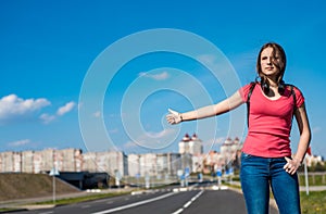 Teenager brunette girl in coral t-shirt with long hair hitchhiking by the roadside. Thumbing a ride. Outdoors vacation.