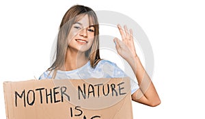 Teenager caucasian girl holding mother nature is crying protest cardboard banner doing ok sign with fingers, smiling friendly