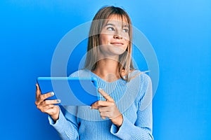 Teenager caucasian girl using touchpad device smiling looking to the side and staring away thinking