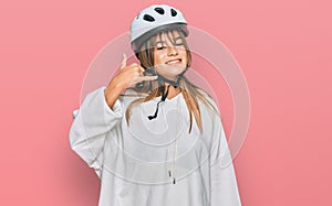 Teenager caucasian girl wearing bike helmet smiling doing phone gesture with hand and fingers like talking on the telephone