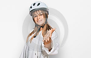 Teenager caucasian girl wearing bike helmet smiling friendly offering handshake as greeting and welcoming