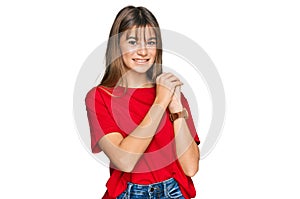 Teenager caucasian girl wearing casual red t shirt laughing nervous and excited with hands on chin looking to the side