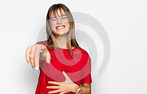 Teenager caucasian girl wearing casual red t shirt laughing at you, pointing finger to the camera with hand over body, shame