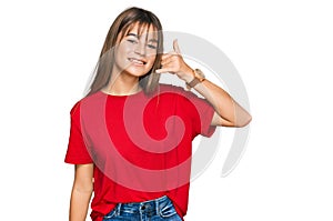 Teenager caucasian girl wearing casual red t shirt smiling doing phone gesture with hand and fingers like talking on the telephone