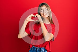 Teenager caucasian girl wearing casual red t shirt smiling in love doing heart symbol shape with hands