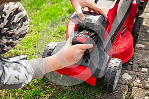 Teenager changes rechargeable battery in electric lawn mower