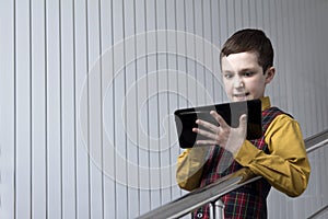 A teenager in a checkered jacket and yellow shirt looks at the tablet irritably while playing or working.
