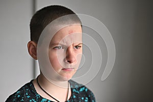 a teenager child with a bruise on his forehead looks angrily against the background of a gray wall. Transitional age