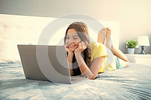 Teenager child girl working on laptop pc computer lying in bed resting relaxing in bedroom at home. teen girl, positive
