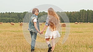 Teenager couple holding hands walking on rural field on haystack background. Romantic girl and boy turning on harvesting