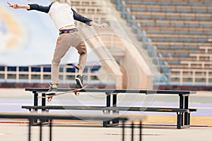 Teenager doing a trick by skateboard on a rail in skate park