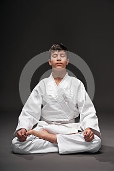 A teenager dressed in martial arts clothing meditating on a dark gray background, a sports concept