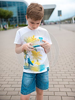 Teenager, dressed in white t-shirt, sits outdoor on skateboard and uses smartphone, digital gadget, plays computer games, browsin
