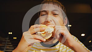 Teenager eating fastfood. Close-up shot of teen boy biting cheeseburger in fast food restaurant.